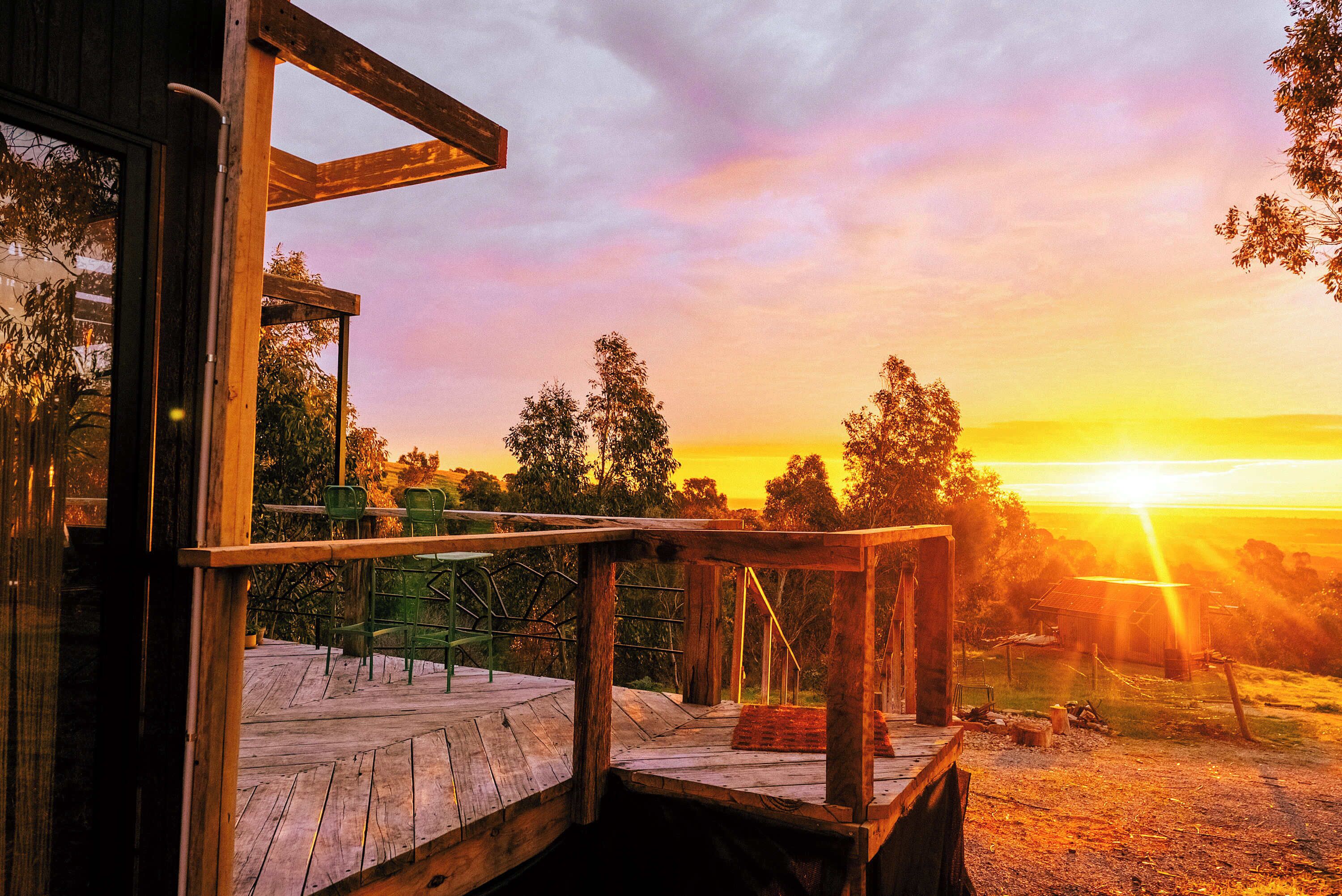 A wooden deck with a view of the sunset and trees.