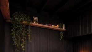 Een gezellige kamer met een rode bank, een zachte witte plaid, een houten plank met boeken en kaarsen, en een klein tafeltje met een kaars en een mok.