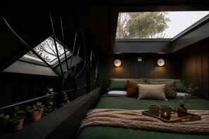 A bedroom with a skylight, a bed with green bedding, bedside lamps, and a tray with mugs.