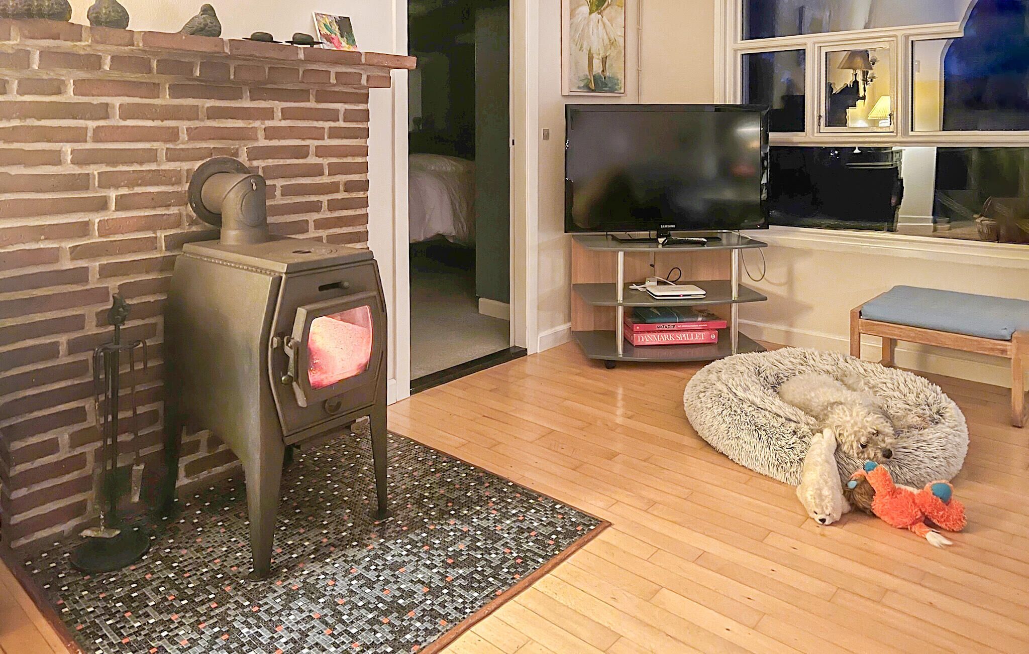 Ein Wohnzimmer mit Kamin aus Ziegelsteinen, einem Fernseher, einem Bücherregal und einem Hund mit Spielzeug.