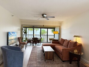 A spacious living room with a sofa, armchair, coffee table, and a television. - Sandpiper Key 2BR Bay Views & Heated Pools (Englewood)