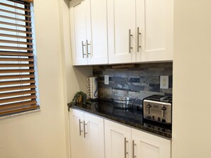 A kitchen with white cabinets, a tiled backsplash, a toaster, and a window with blinds. - Sandpiper Key 2BR Bay Views & Heated Pools (Englewood)