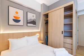 Ein modernes Hotelzimmer mit einem Bett, einem Kleiderschrank und zwei gerahmten Kunstwerken an der Wand.