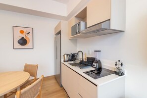 Eine kompakte Küche mit Herd, Wasserkocher und Mixer, ein Essbereich mit Tisch und Stühlen und eine Mikrowelle über der Arbeitsfläche.