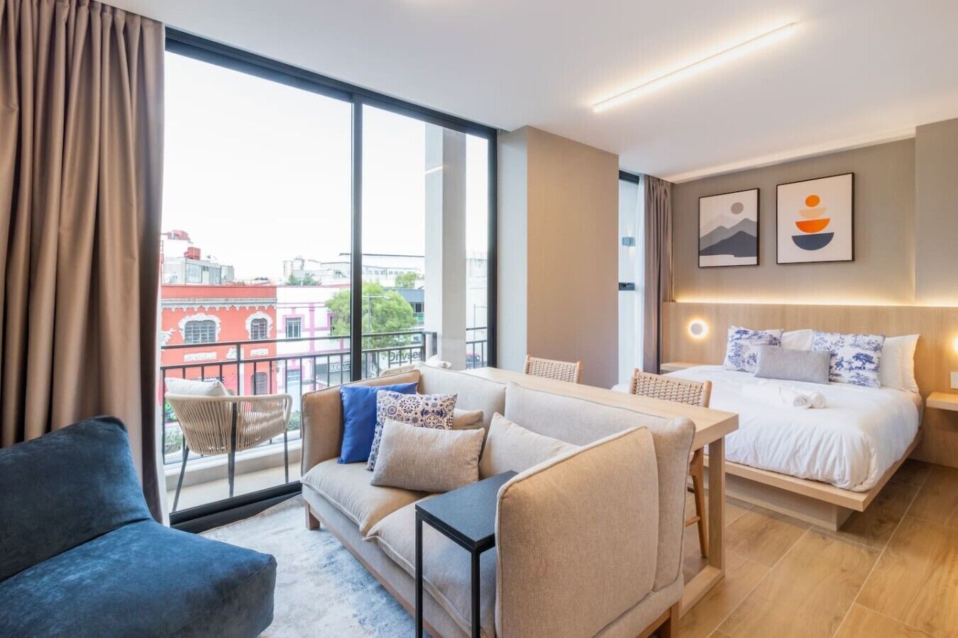 A modern hotel room with a balcony, a bed, a sofa, and a dining table.