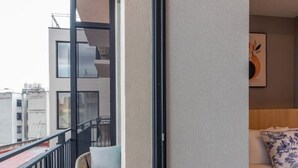 Parveke, jossa on oleskelualue, kuviollinen koristetyyny sängyllä ja näkymä kaupunkiin.