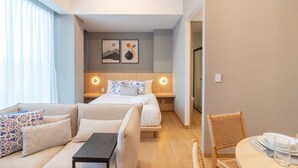 Moderni hotellihuone, jossa on sänky, sohva, ruokapöytä ja pieni pöytä.