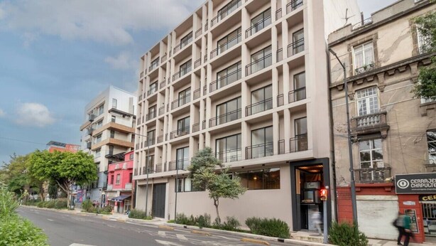 Un hôtel à plusieurs étages, doté de balcons, d’une entrée bien visible et donnant sur la rue, avec d’autres bâtiments en vue.