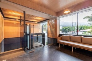 Ein modernes Interieur mit einem gläsernen Aufzug, einer Sitzbank und Blick ins Freie.