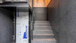 Un escalier avec une rampe, un ascenseur en verre et un mur orné de lambris en bois.