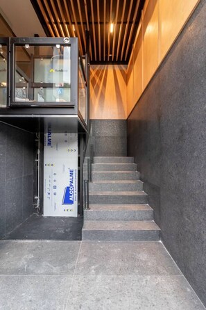 Eine Treppe mit Handlauf, ein Glaselevator und eine Wand mit Holzlamellen.