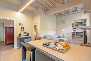 A modern kitchen with a dining area, a coffee station, and a living space with a sofa and a TV. - Boutique Apartment, Toscolano Maderno, Italy (Toscolano Maderno)