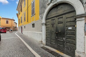 A cobblestone street with a yellow building, a red car, and a large wooden door. - Boutique Apartment, Toscolano Maderno, Italy (Toscolano Maderno)