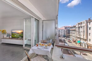 A balcony with a dining table set for two, a television, and a vase with flowers. - Le Plaza Antibes, Antibes, France (Antibes)