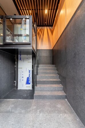 Eine moderne Treppe mit einem gläsernen Aufzug auf der linken Seite und einer Holzdielendecke.