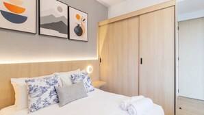 Ein Hotelzimmer mit Bett, Kissen, einem Nachttisch, einer Wandleuchte und einem Holzschrank.