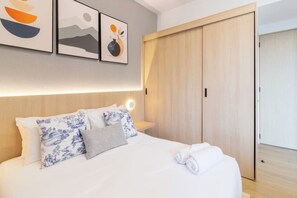 Ein Hotelzimmer mit Bett, Kissen, einem Nachttisch, einer Wandleuchte und einem Holzschrank.