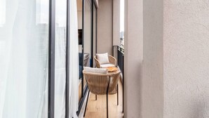 Ein Balkon mit Korbstuhl, kleinem Tisch, Stadtblick und großem Fenster.