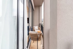 Ein Balkon mit Korbstuhl, kleinem Tisch, Stadtblick und großem Fenster.