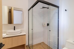 Ein modernes Badezimmer mit einer Duschkabine aus Glas, einem weißen Waschbecken und einem Holz-Waschtisch.