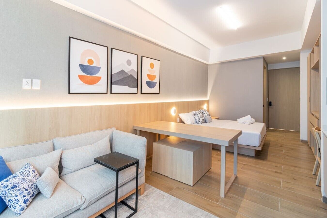 Una camera moderna e luminosa con un divano, un tavolino e un letto. In parete, tre opere d'arte incorniciate.