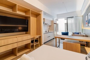 Ein moderner, gut beleuchteter Raum mit einem Holztisch, einem Fernseher, einem Essbereich und einer Küche im Hintergrund.