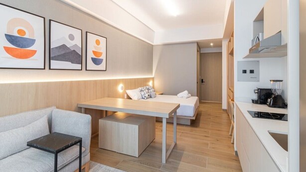 Ein modernes Hotelzimmer mit einer Couch, einem Bett, einem Schreibtisch und einer Küchenzeile.