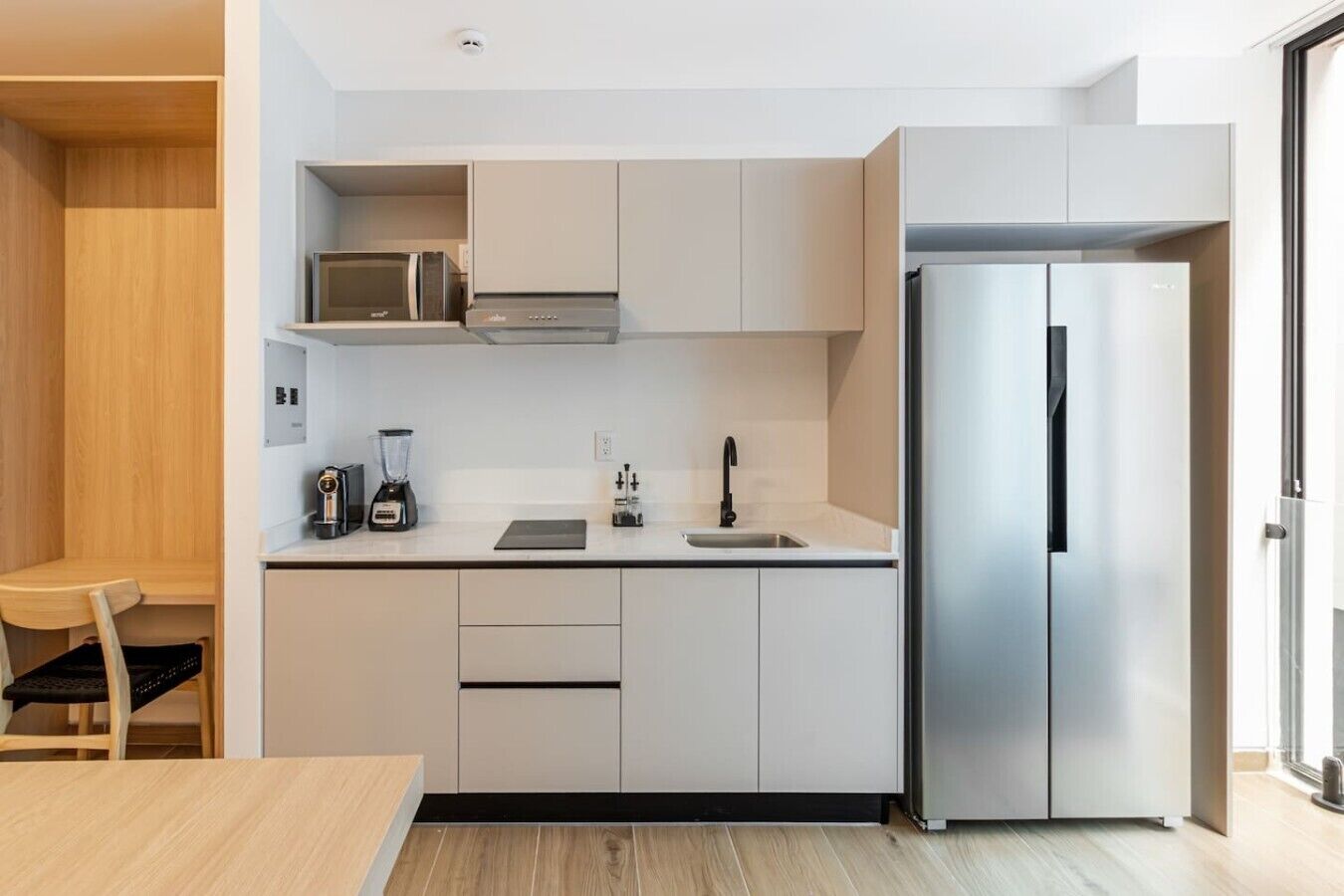 Eine moderne Küche mit weißen Schränken, einem Edelstahl-Kühlschrank, einer Mikrowelle und einem Mixer auf der Arbeitsfläche.