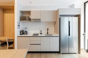 Eine moderne Küche mit weißen Schränken, einem Edelstahl-Kühlschrank, einer Mikrowelle und einem Mixer auf der Arbeitsfläche.