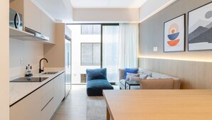 Eine moderne Küche mit Einbauherd, ein Essbereich mit Holztisch und eine Couch. Ein großes Fenster lässt natürliches Licht herein und bietet einen Blick ins Freie.