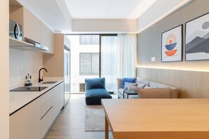Eine moderne Küche mit Einbauherd, ein Essbereich mit Holztisch und eine Couch. Ein großes Fenster lässt natürliches Licht herein und bietet einen Blick ins Freie.