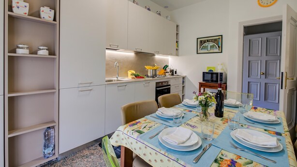 Un coin repas avec une table dressée pour quatre personnes, une cuisine en arrière-plan et une porte avec une pancarte.