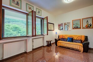 A room with a sofa, a radiator, a window with a view of greenery, and framed pictures on the wall. - Il Paradiso è Qui! Nel silenzio col mare a due passi, Sestri Levante, Italy (Sestri Levante)