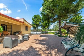 Eine Terrasse mit Gartenmöbeln, ein Gebäude mit rotem Dach und umliegende Bäume.