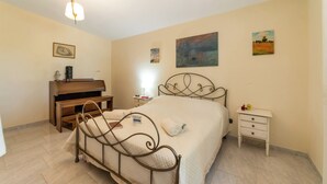Quarto com estrutura de cama de metal, mesa de cabeceira de madeira, mesa de apoio branca e luminária na parede.