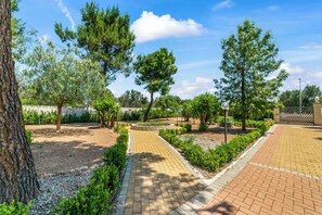 Un sendero pavimentado, árboles y un jardín circular en un área ajardinada.