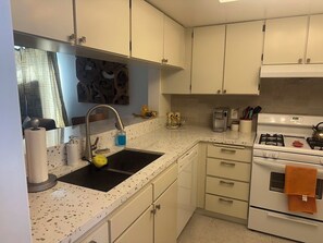 A kitchen with white cabinets, a black sink, a stove, and a dishwasher. - Cozy 1-bedroom condo in fabulous Palm Springs with AC (Palm Springs)