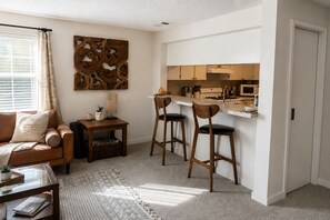 Un espace de vie compact comprenant un coin cuisine, un canapé, une table basse et un tapis à motifs.
