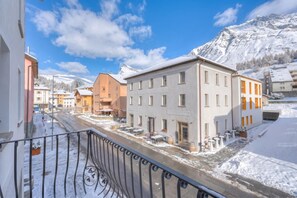 A snow-covered street with buildings, including a two-story building with a balcony. - Residenza Tilia 202 San Bernardino Swiss Alps, San Bernardino, Switzerland (San Bernardino)