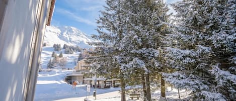 A snowy landscape with a mountain in the background, a building with a sign, and snow-covered trees.