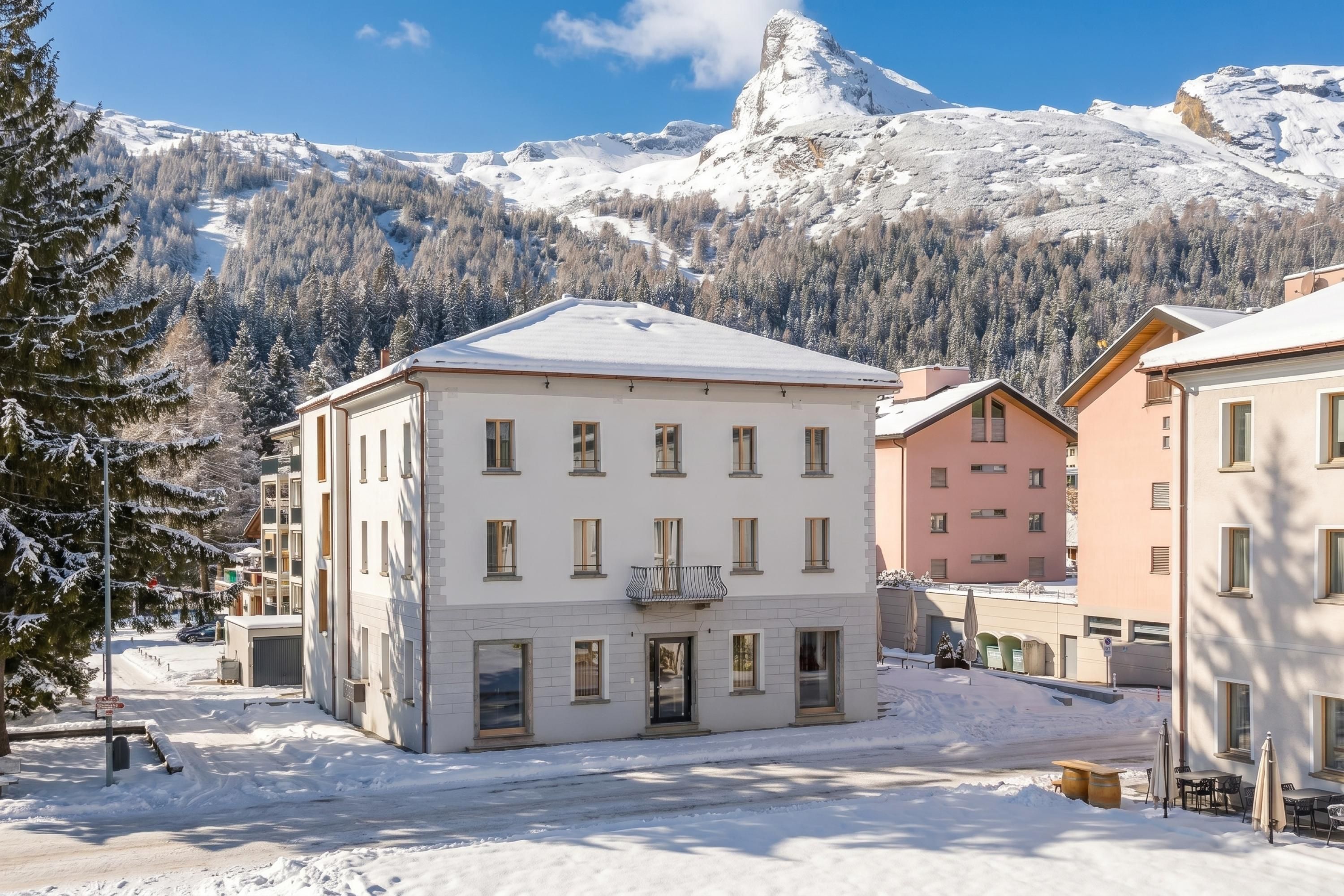 A snow-covered building with a symmetrical facade, large windows, and a flat roof, surrounded by snow-laden trees and mountains.