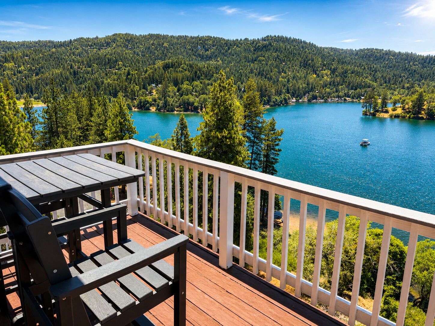 A wooden deck with a table and chairs overlooking a lake surrounded by trees and hills.