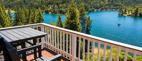 A wooden deck with a table and chairs overlooking a lake surrounded by trees and hills.