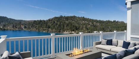A terrace with a fire pit, outdoor seating, and a view of a lake and forested hills.
