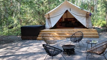 Een tent met een houten terras en zitgedeelte, omringd door bomen.