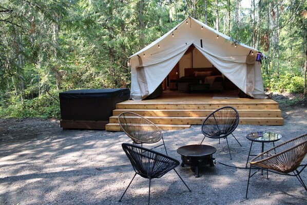 A tent with a wooden deck and seating area, surrounded by trees.