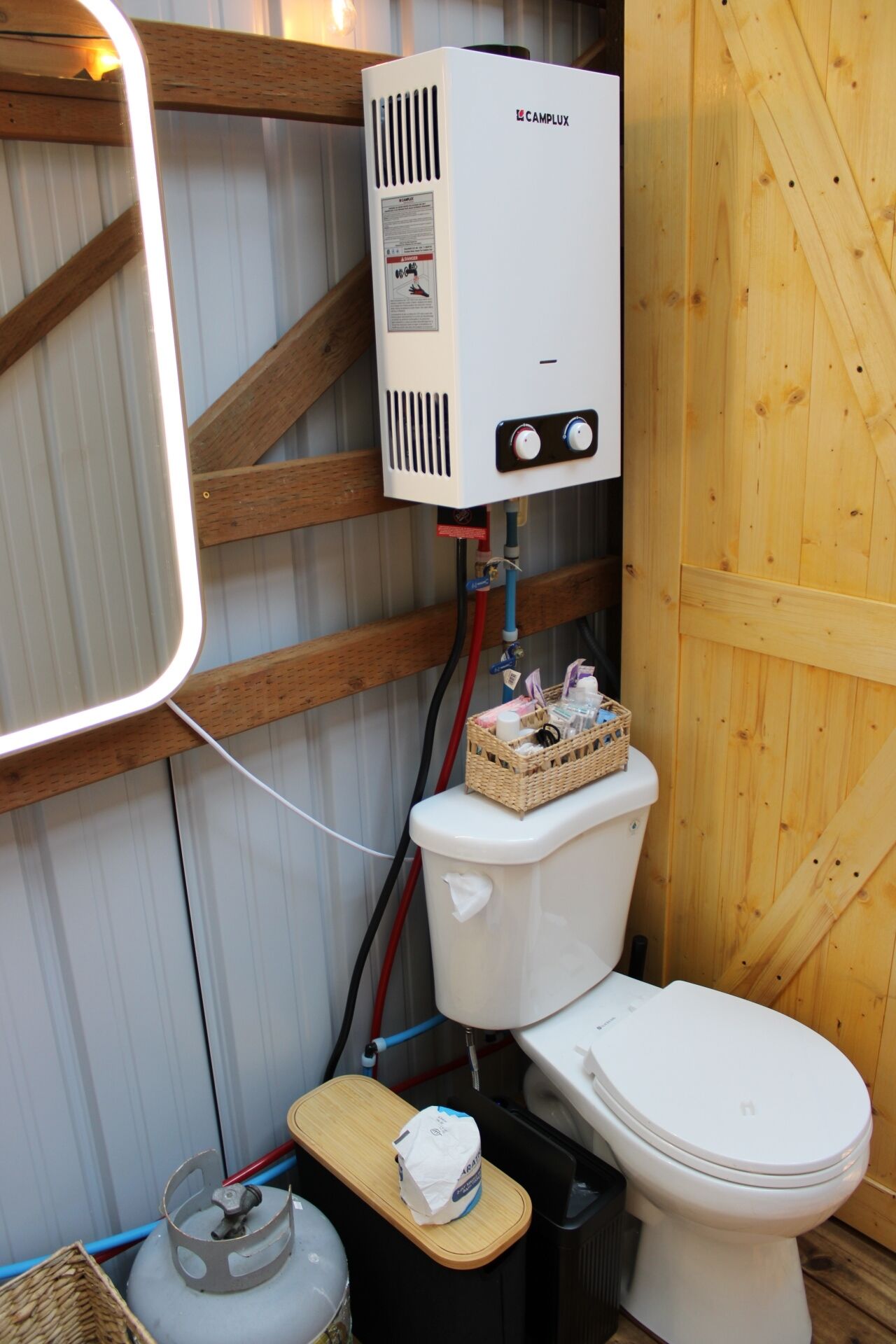 A compact bathroom with a white toilet, a white heater labeled CAMPLUX, and a wooden wall.
