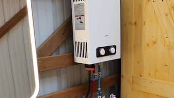 A compact bathroom with a white toilet, a white heater labeled CAMPLUX, and a wooden wall.