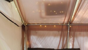 A tent with a cushioned seating area, a wooden floor, and string lights.