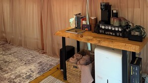 A tented room with a table, books, a coffee maker, and a small refrigerator.